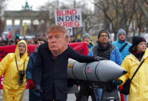 An anti-war protester wears a mask showing US President Donald Trump in Berlin, Germany, Saturday, Nov. 18, 2017 during a demonstration against nuclear weapons near the Brandenburg Gate. (Michael Sohn/Associated Press)