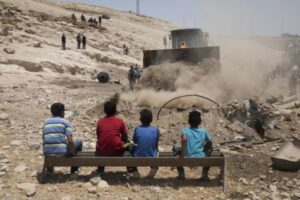 Children watch an Israeli army bulldozer preparing the ground for the demolition of the Palestinian Bedouin village of Khan al-Amar, in the occupied West Bank on July 4, 2018. (Activestills/Oren Ziv)