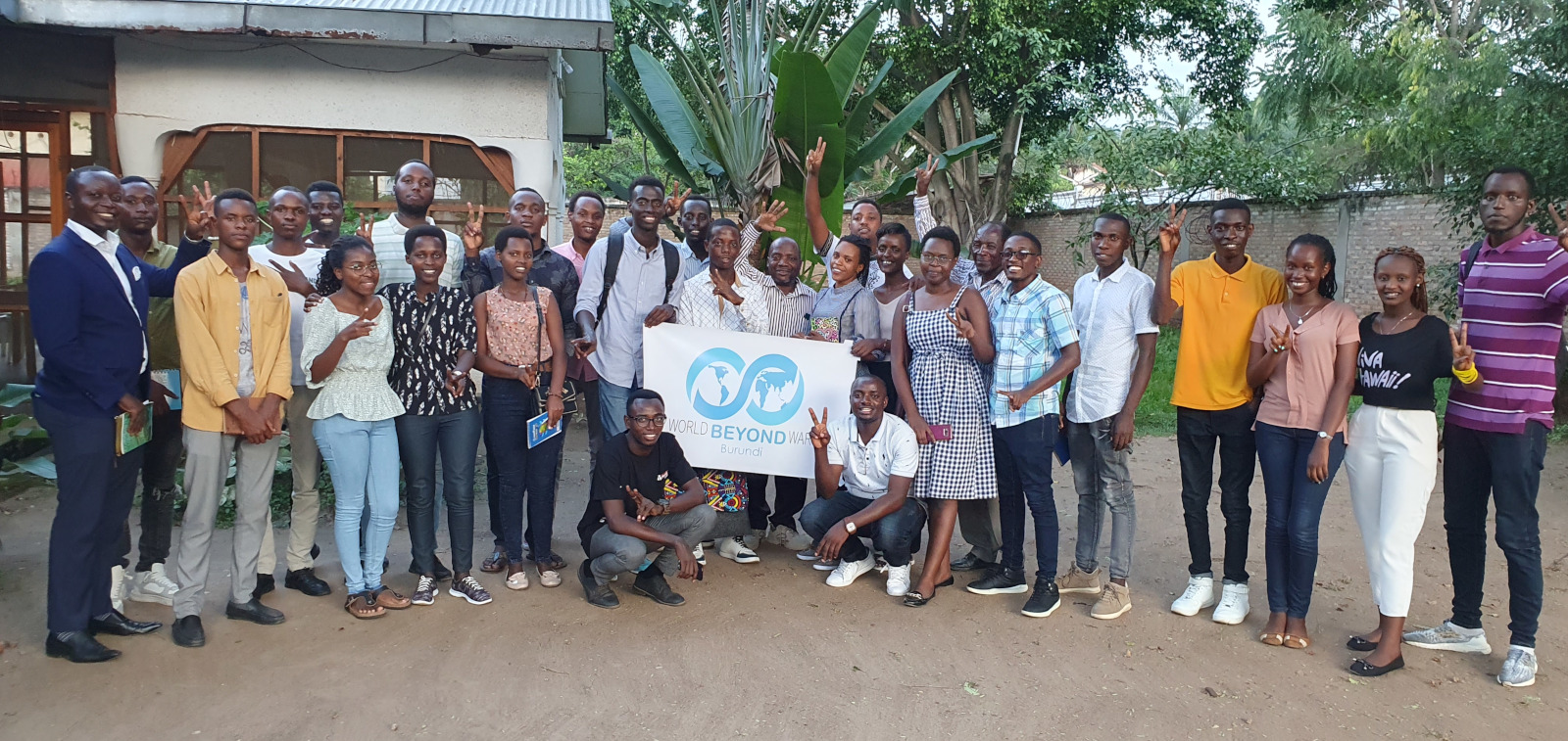 Alrededor de 30 miembros del capítulo de Burundi se paran en un semicírculo, posando para la foto, sosteniendo una pancarta de WBW.