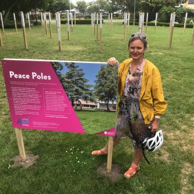 New Zealand chapter coordinator Liz Remmerswaal standing by the plaque commemorating the peace poles