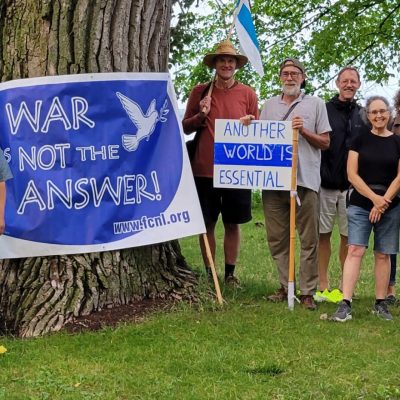 Members of the Madison chapter stand on a grassy lawn in front of a large tree, holding up a big banner reading "War is not the answer"